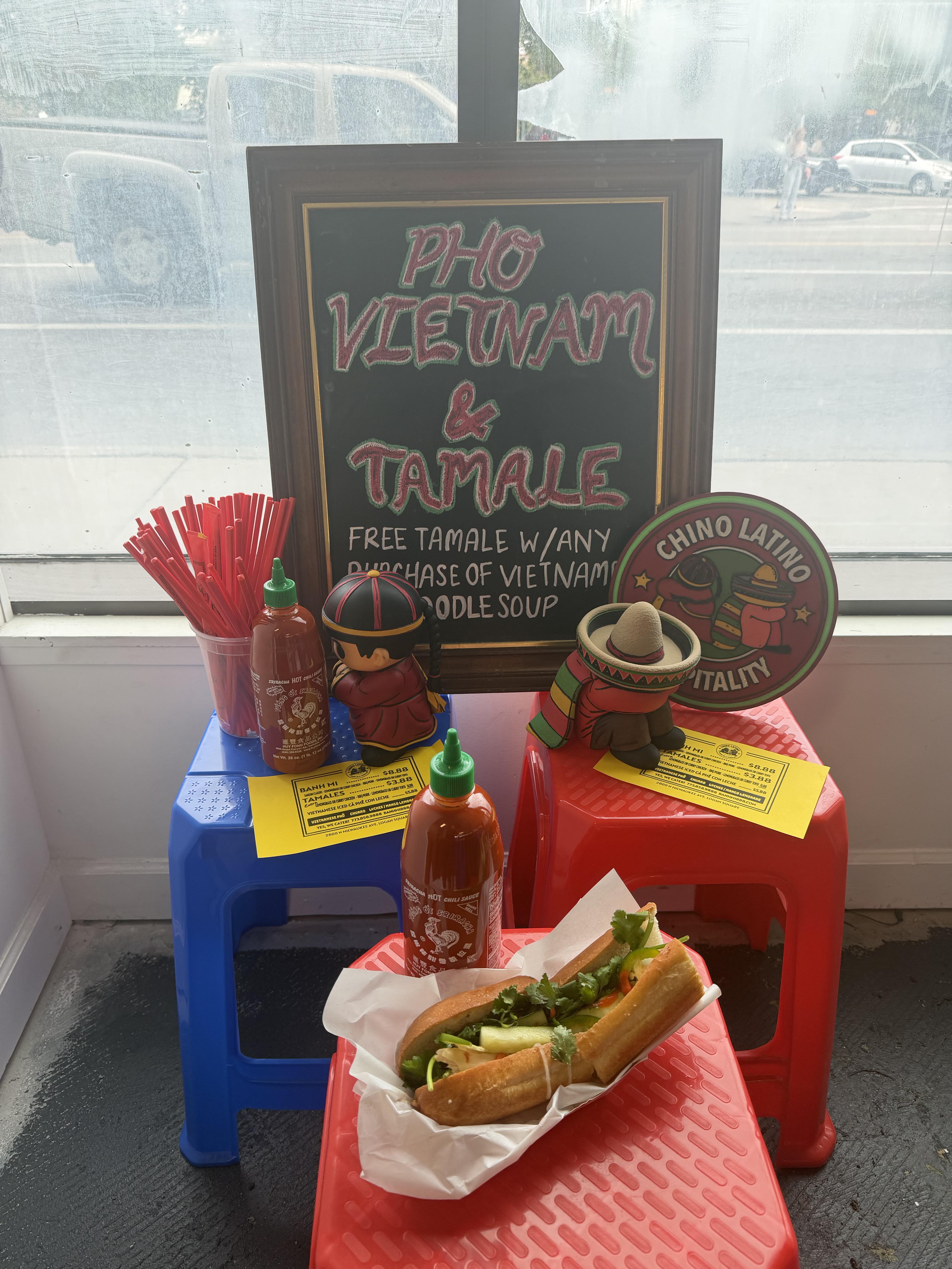 A bánh mì sandwich beside colorful stools and a restaurant chalkboard